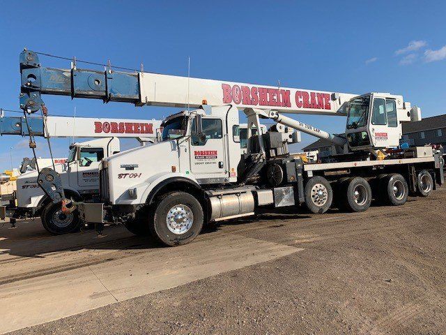 A white truck with a crane on the back is parked in a parking lot.