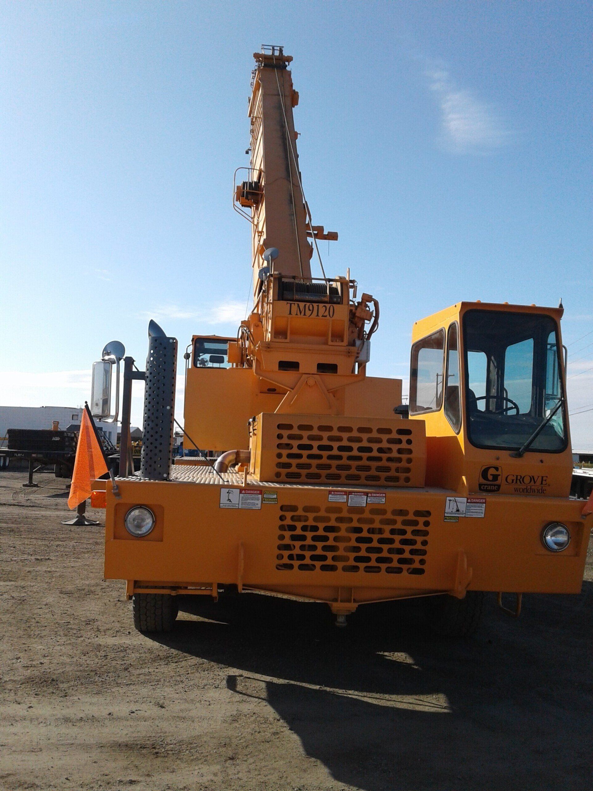 A yellow truck with a crane on the back is parked in a dirt field