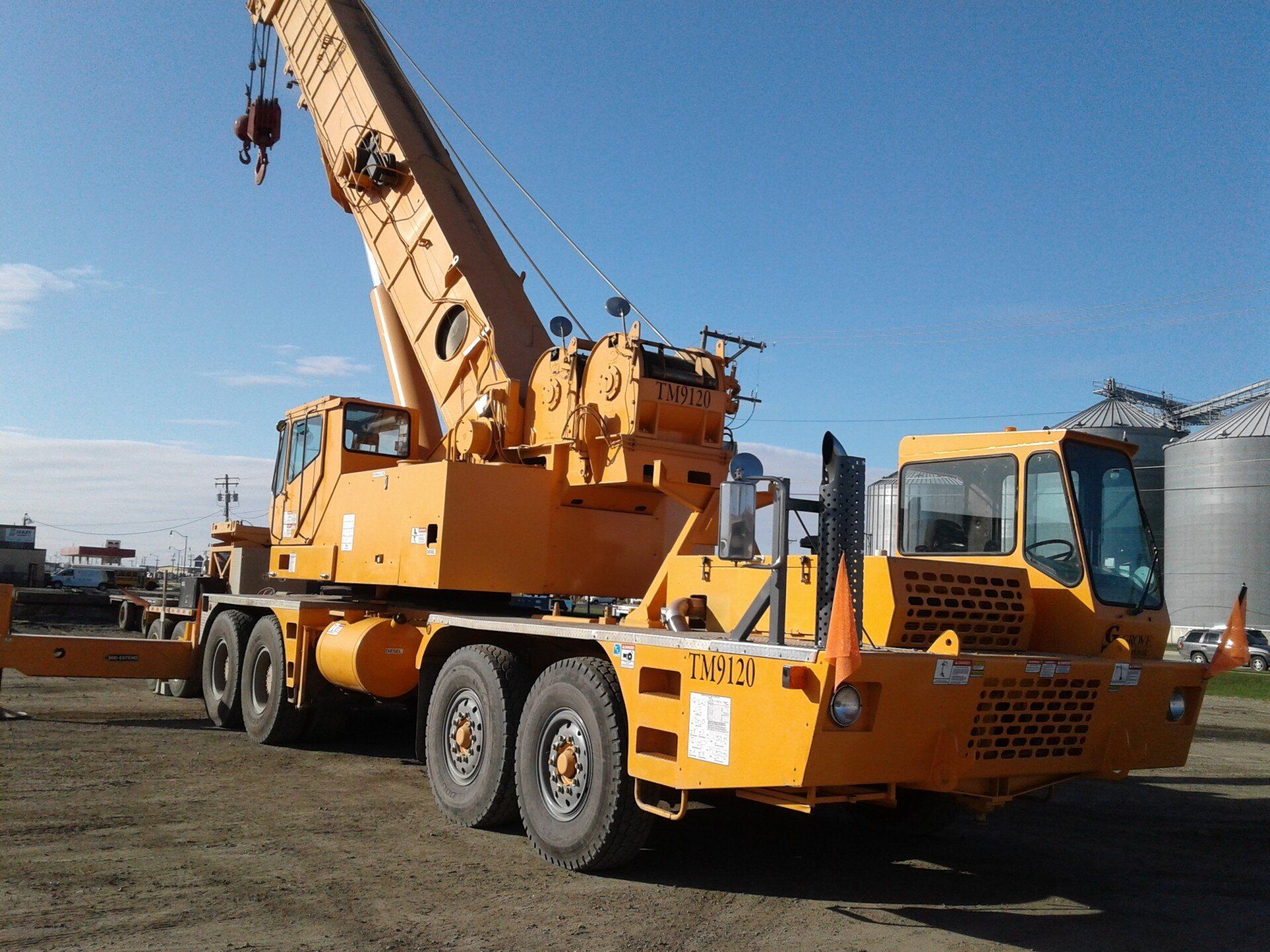 A large yellow crane is parked in a dirt lot