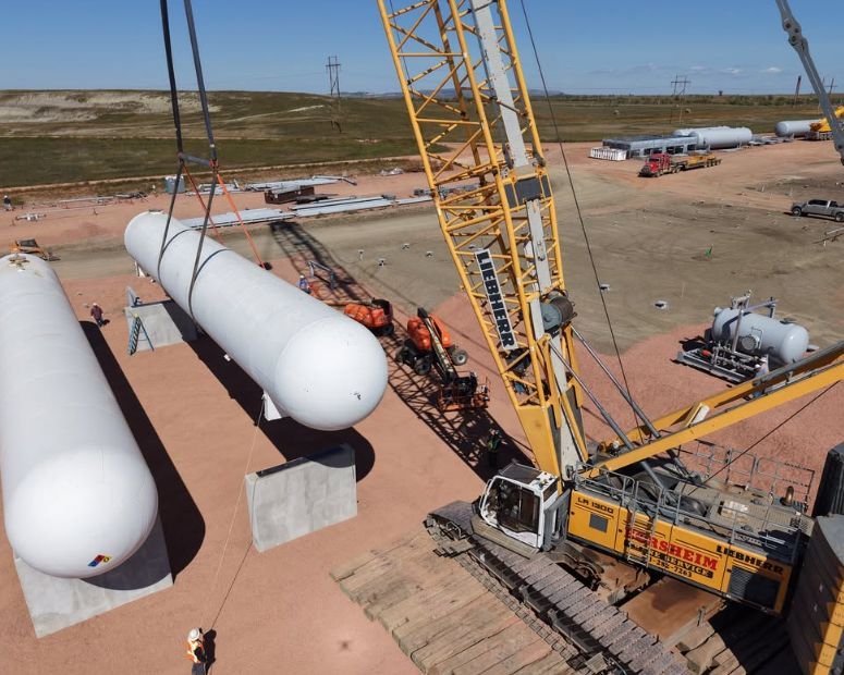 A large crane lifting a white cylindrical tank at a construction site.