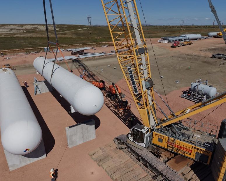 A large crane lifting a white cylindrical tank at a construction site.