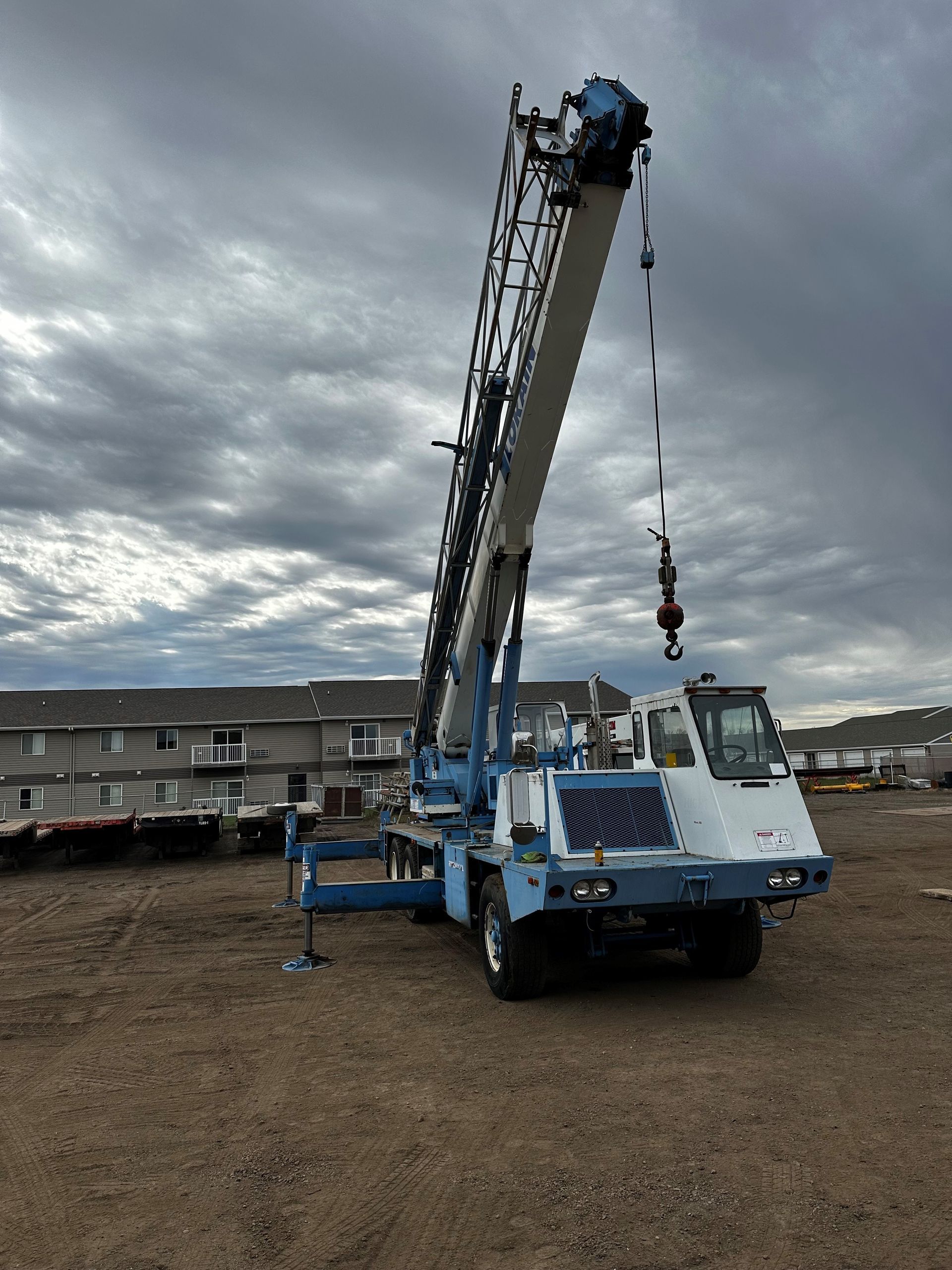 A blue and white crane is parked in a gravel lot