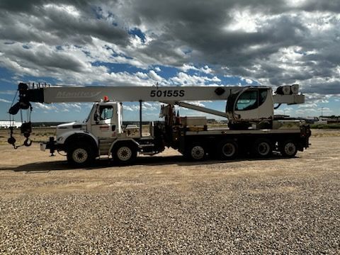 A large crane truck is parked in a gravel lot.