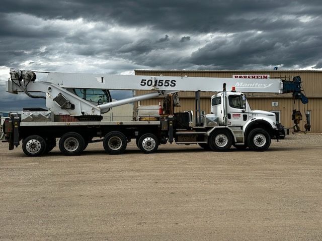 A white truck with a crane attached to it is parked in front of a building.