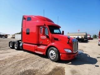 A red semi truck is parked in a dirt lot.