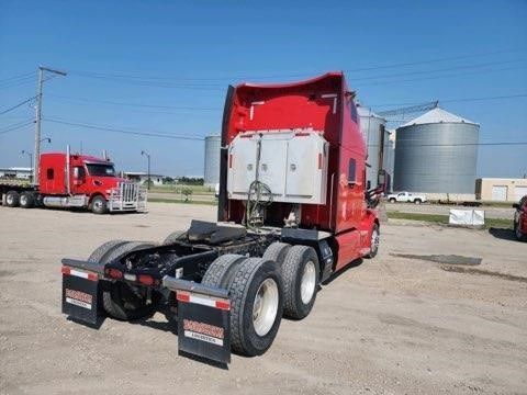 A red semi truck is parked in a dirt lot.
