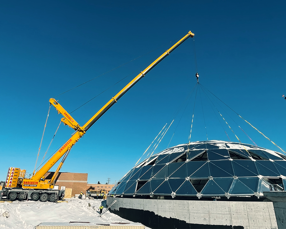 A large yellow crane is working on a dome