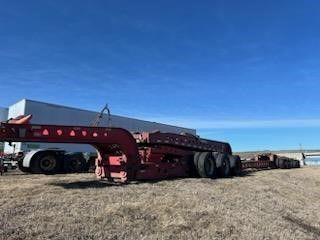 A red trailer is parked in a field in front of a building.