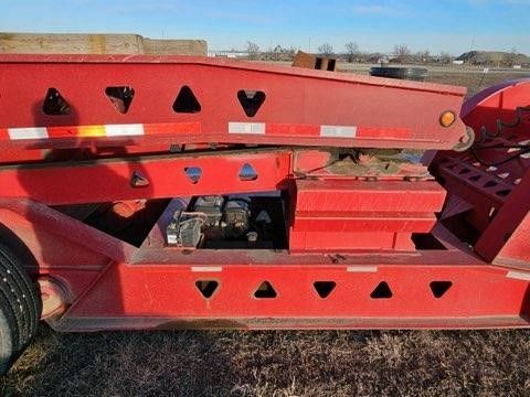 A red trailer is parked in a field with a blue sky in the background.