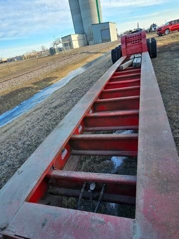 A red trailer is parked on the side of the road in a field.
