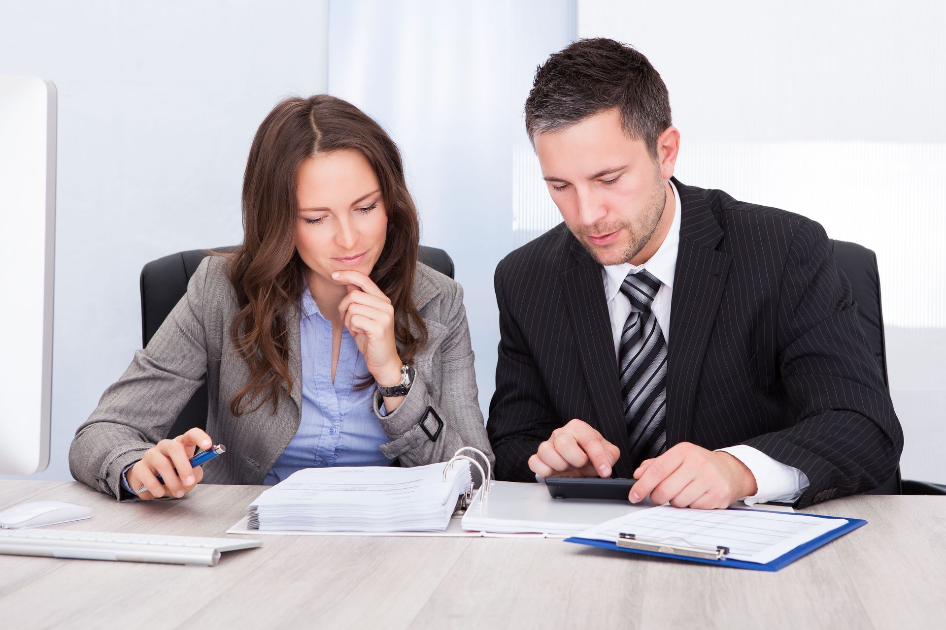 Two business professionals reviewing documents at a desk, one using a calculator.