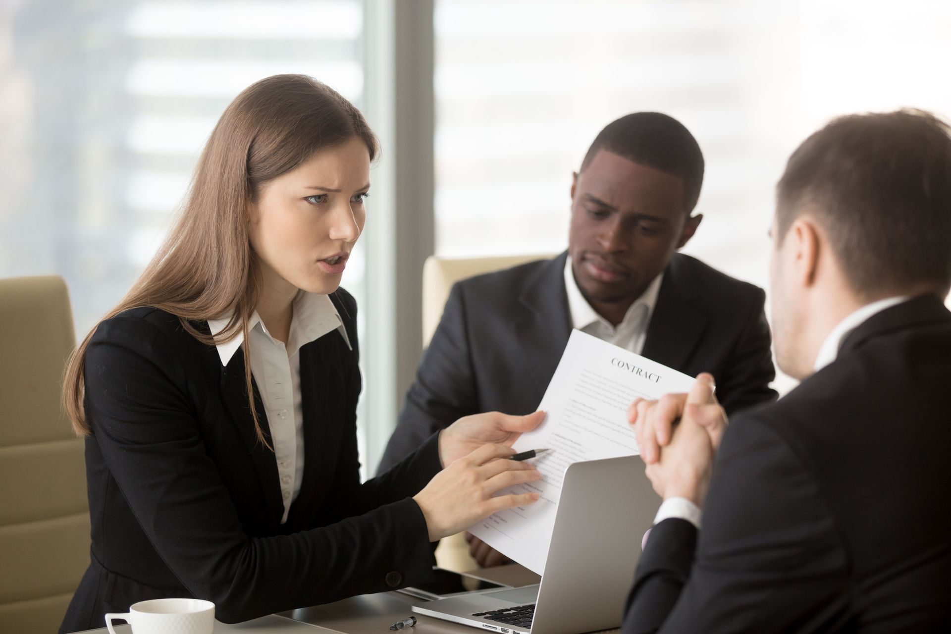 Business meeting with woman pointing at document, man listening, and another man looking on.
