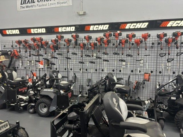A retail store wall displaying numerous Echo brand string trimmers, with several lawn mowers parked in the foreground. 
