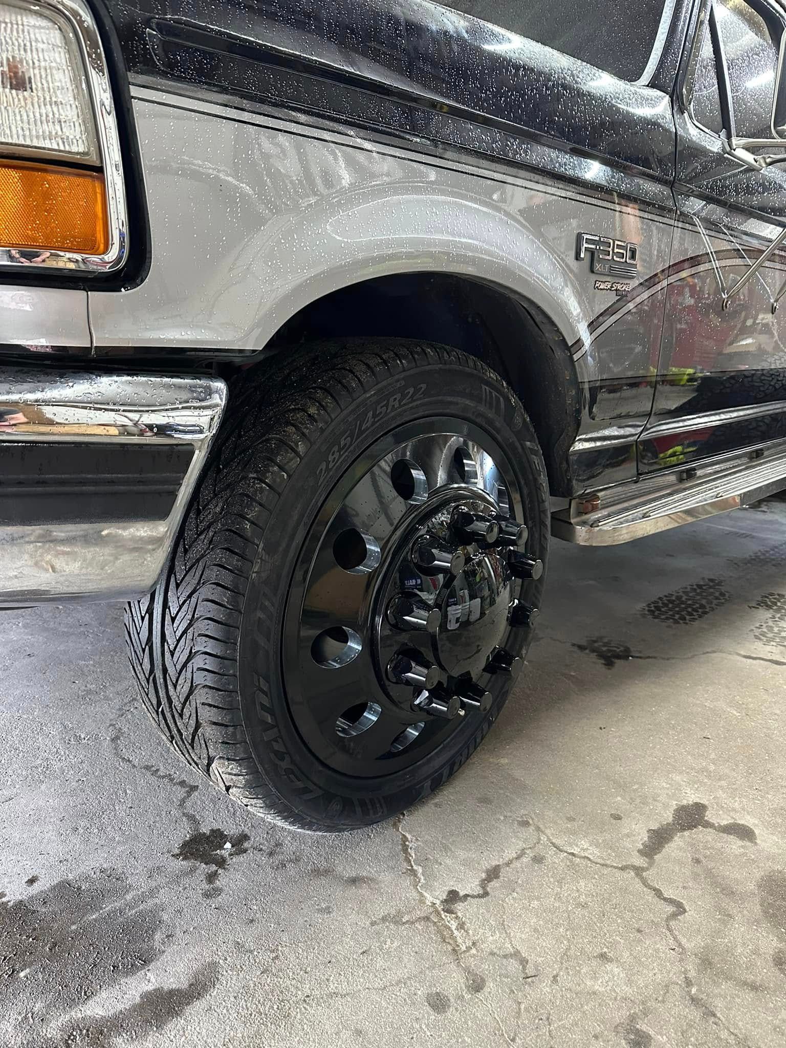A black truck with black wheels and tires is parked on the side of the road.