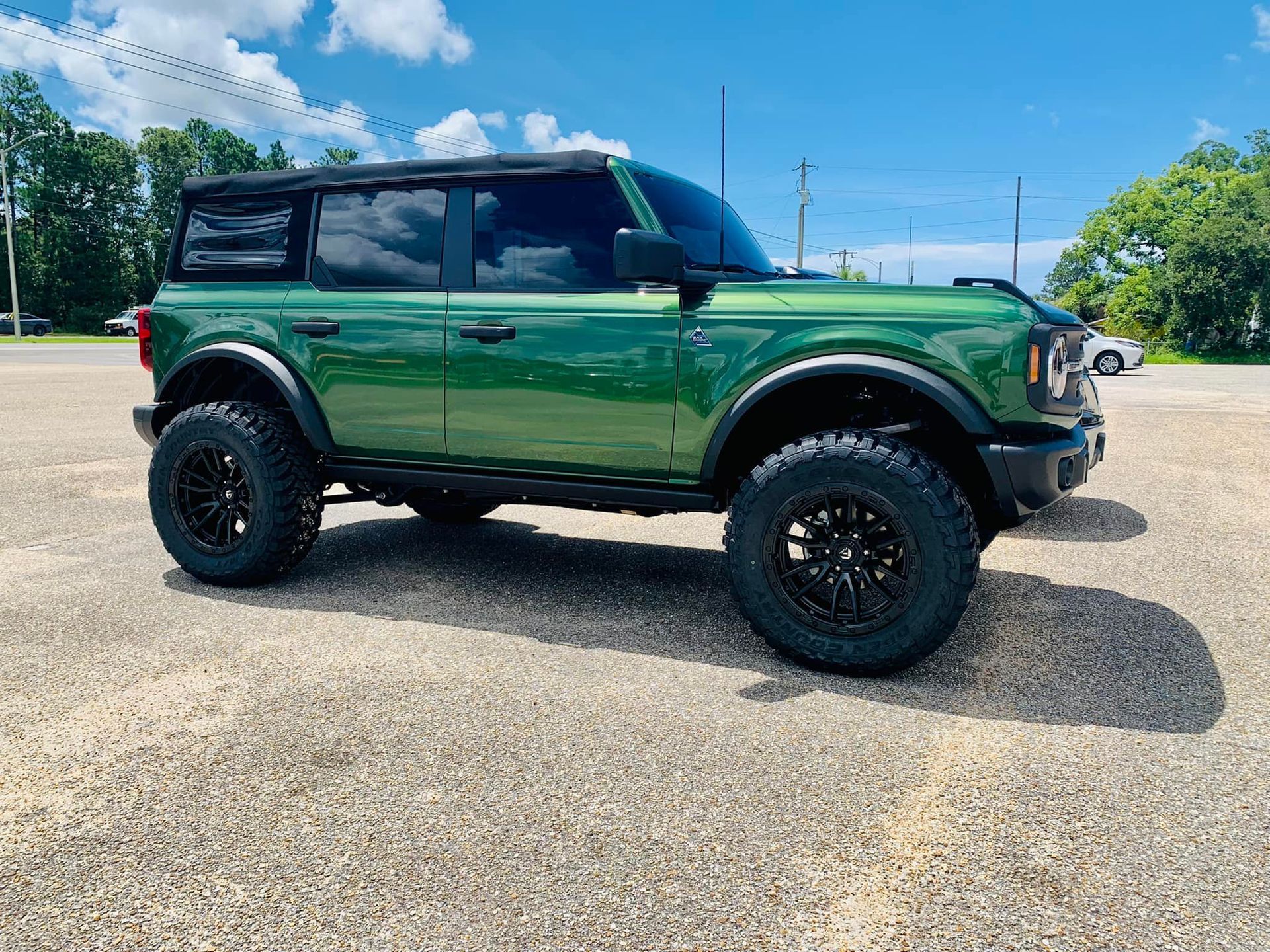 A green Ford Bronco is parked in a gravel lot.