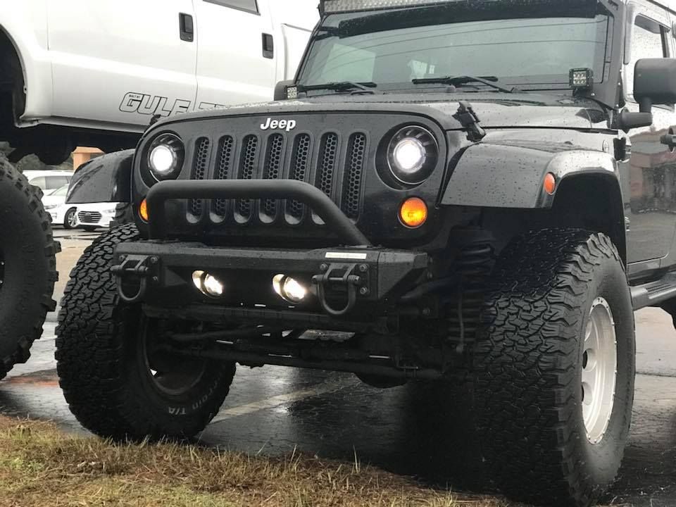 A black jeep is parked in a parking lot next to a white truck.