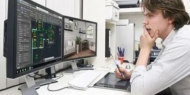 A person contemplates design work on dual monitors, holding a stylus, seated at a desk.