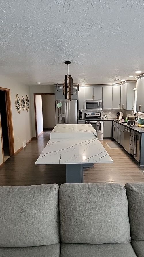 Kitchen with large white countertop island, gray cabinets, stainless steel appliances, and wood floor.