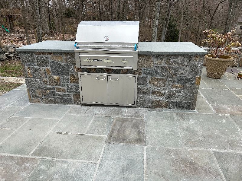 A stainless steel grill is built into a stone wall on a patio.