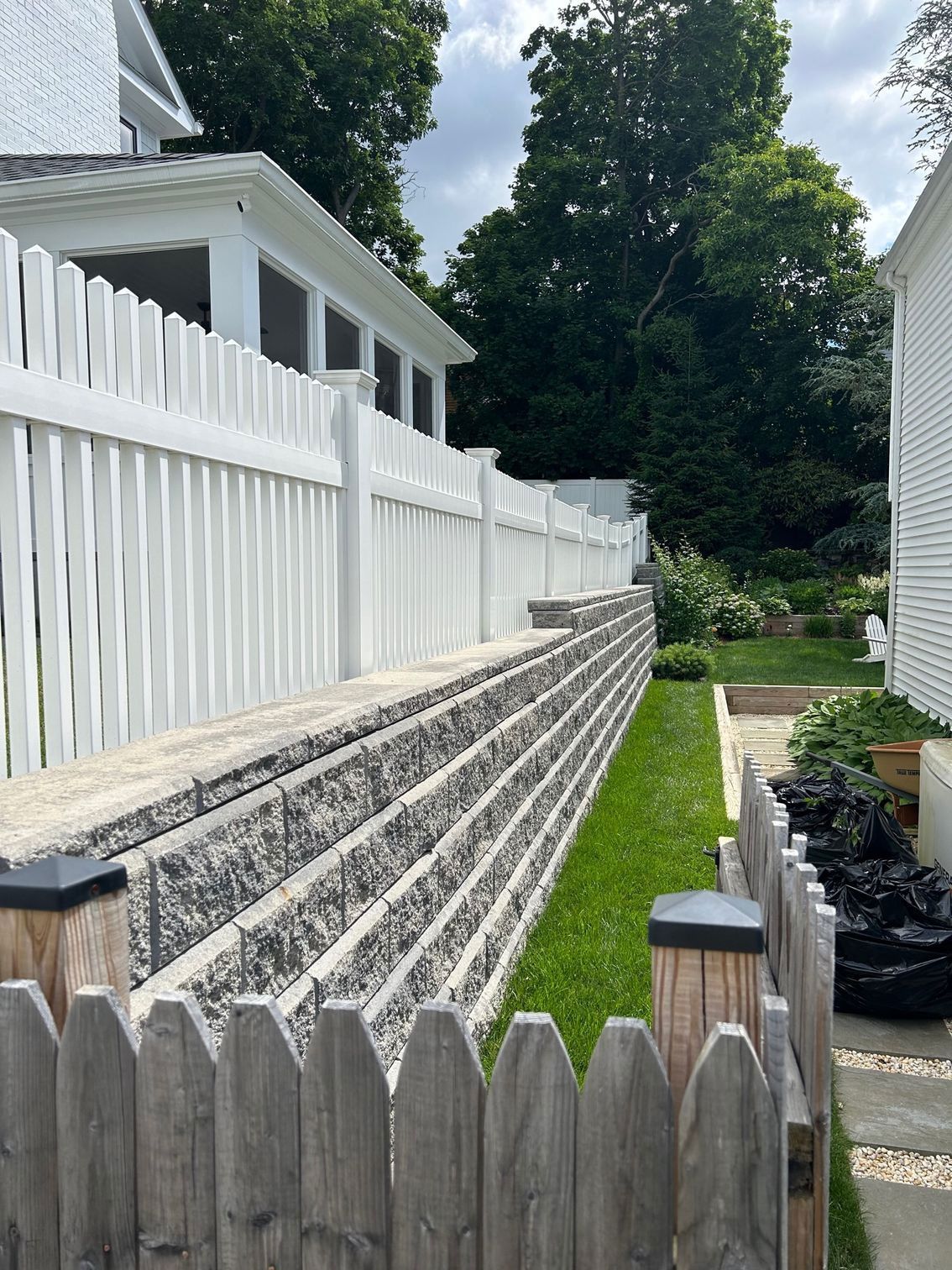 A white picket fence surrounds a stone wall in front of a house.