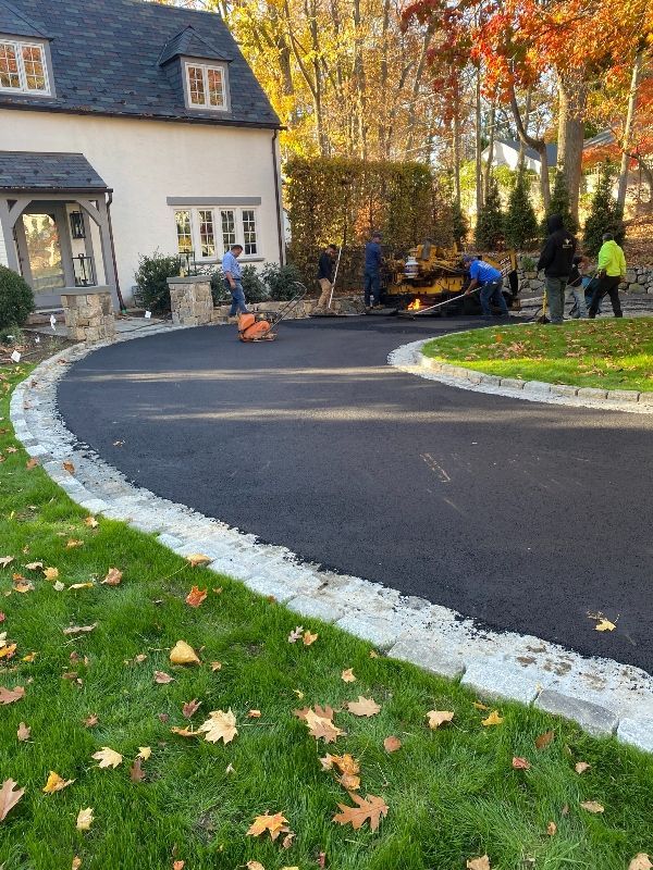 A group of people are working on a driveway in front of a house.