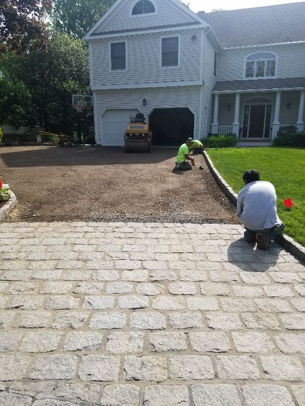 Two men are working on a driveway in front of a house