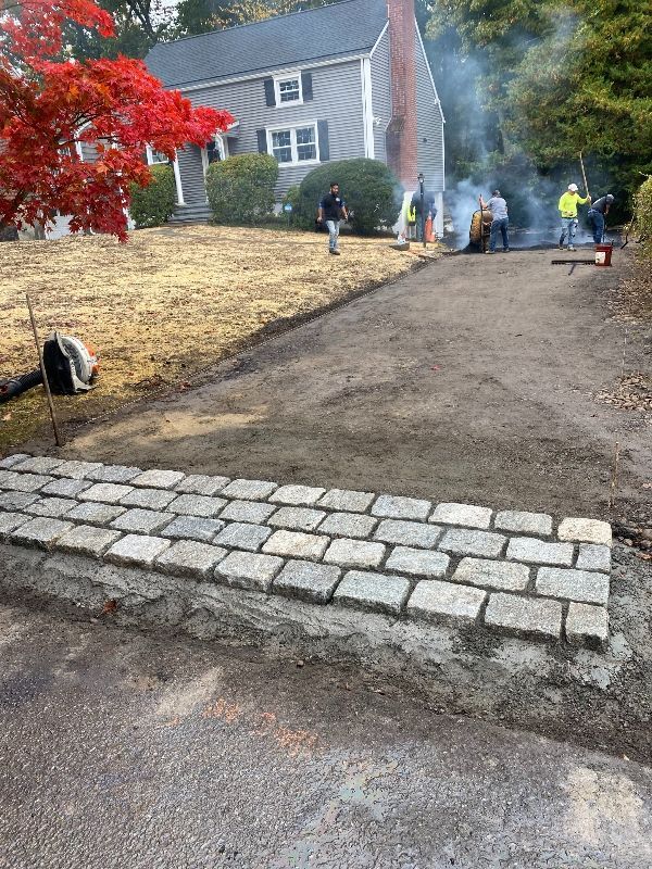 A group of people are working on a driveway in front of a house.