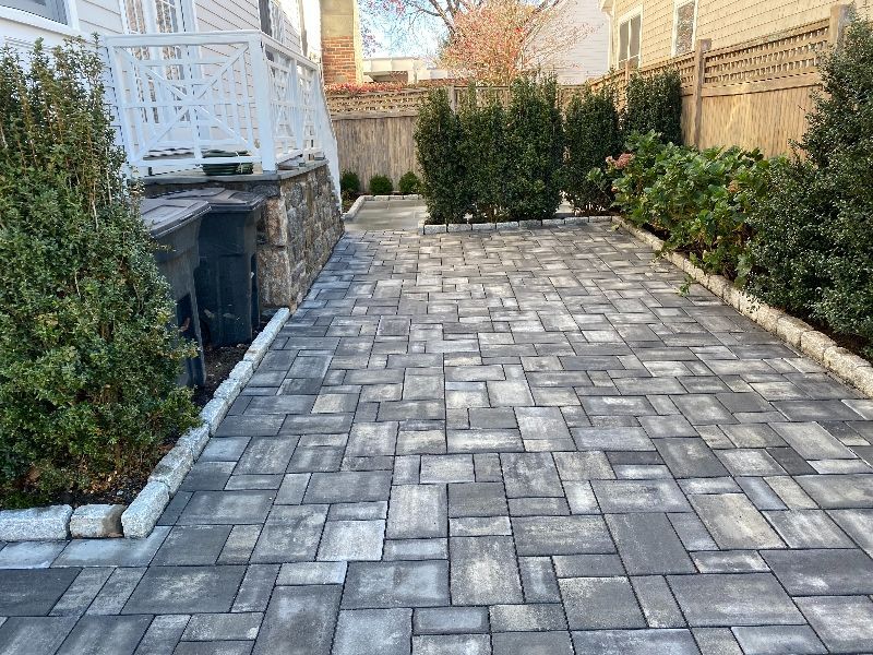 A brick driveway leading to a house with a fence and bushes.