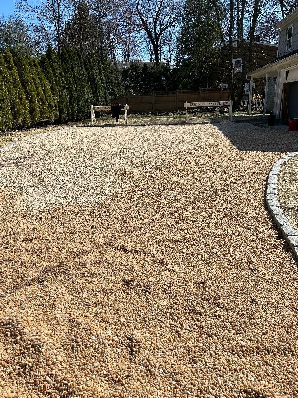 A gravel driveway leading to a house with trees in the background.