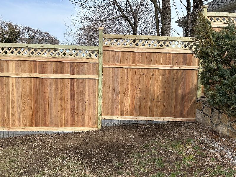 A wooden fence is sitting in the middle of a yard next to a stone wall.
