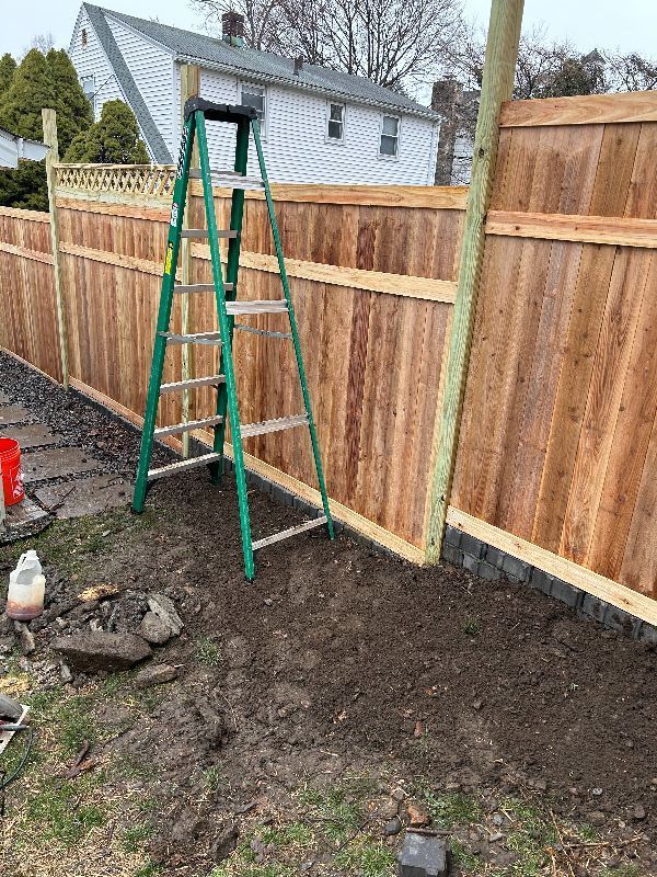 A ladder is sitting next to a wooden fence in a yard.