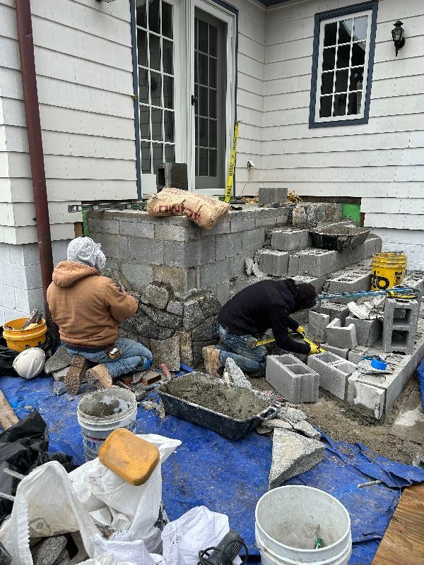 A couple of men are kneeling on a blue tarp in front of a house.