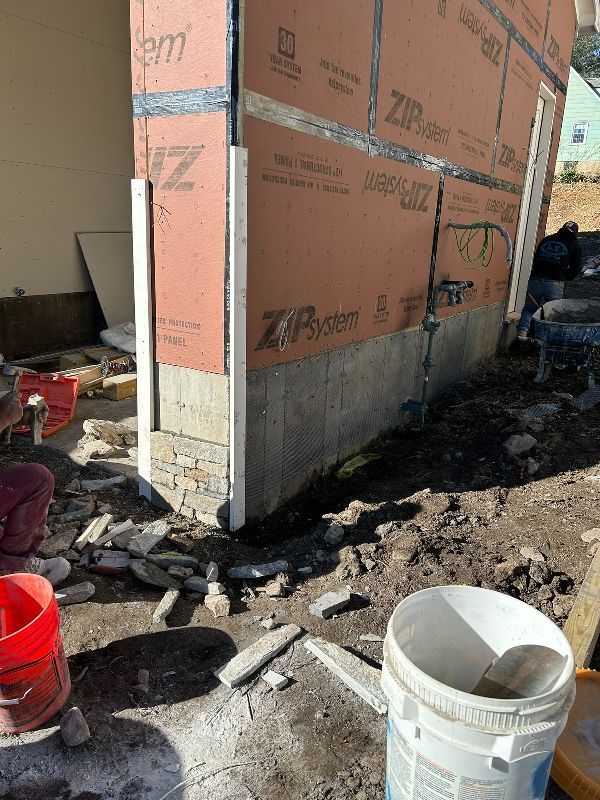 A bucket of cement is sitting in front of a building under construction.
