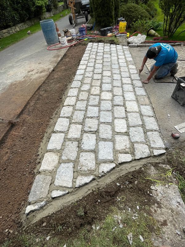 A man is laying bricks on a sidewalk.