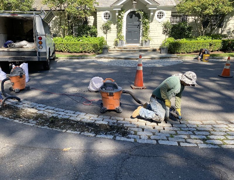 A man is working on a cobblestone driveway in front of a house.