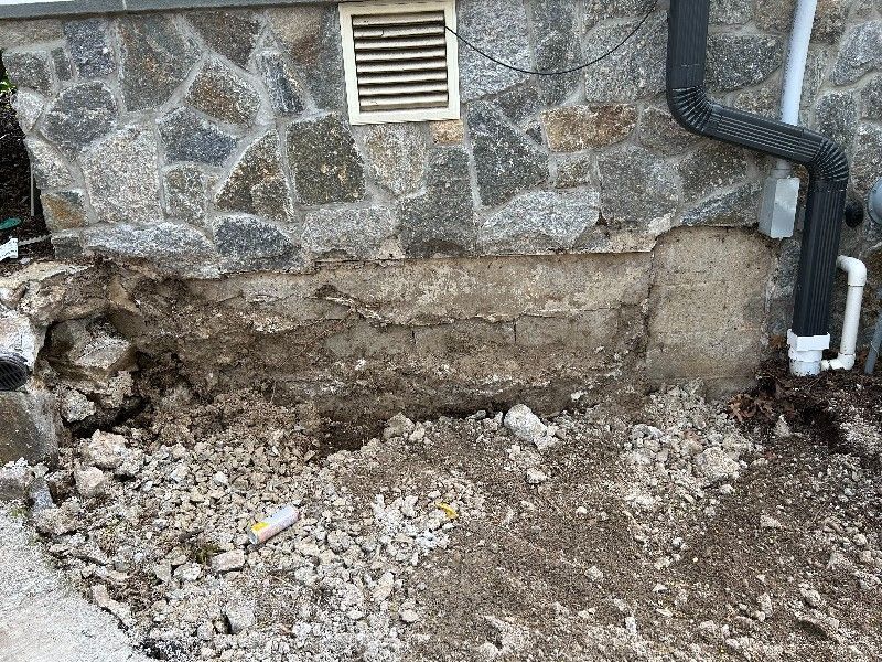 There is a hole in the ground in front of a stone wall.