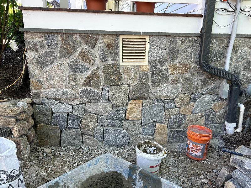 A stone wall is being built next to a bucket of cement.