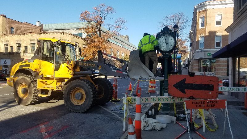 A group of construction workers are working on a street clock.