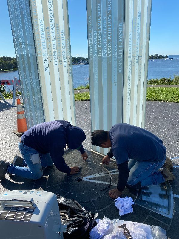 Two men are working on a memorial in front of a body of water.