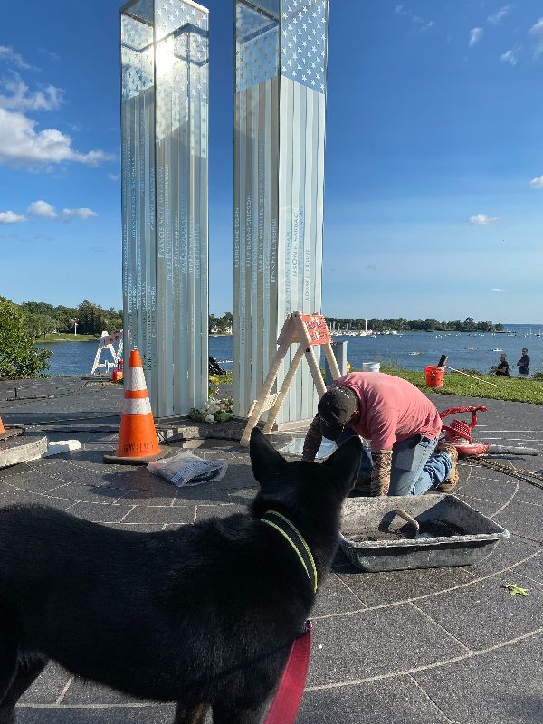 A black dog is looking at a man working on a sculpture.
