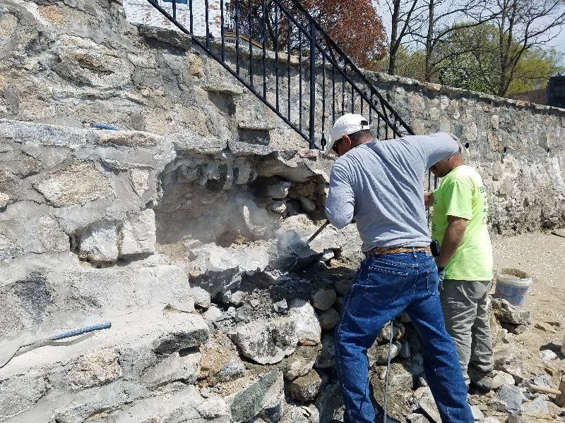 Two men are working on a stone wall next to stairs.