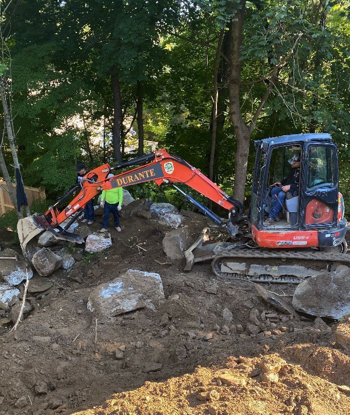 A man in a yellow vest is standing next to an orange excavator that says' demolition' on it