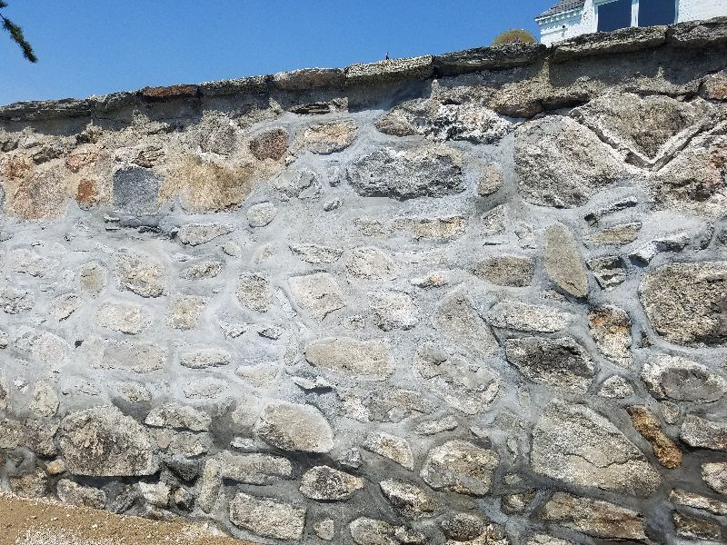 A large stone wall with a house in the background