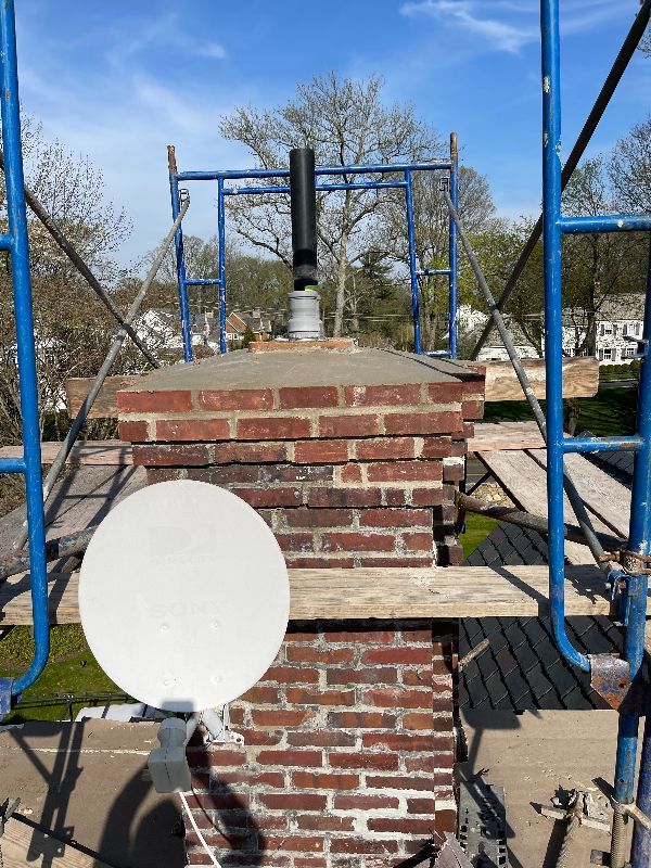 A brick chimney is being repaired on a roof with scaffolding.