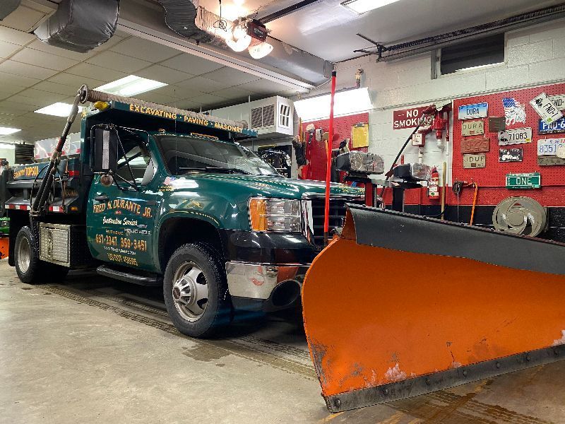 A snow plow is parked in a garage next to a dump truck.