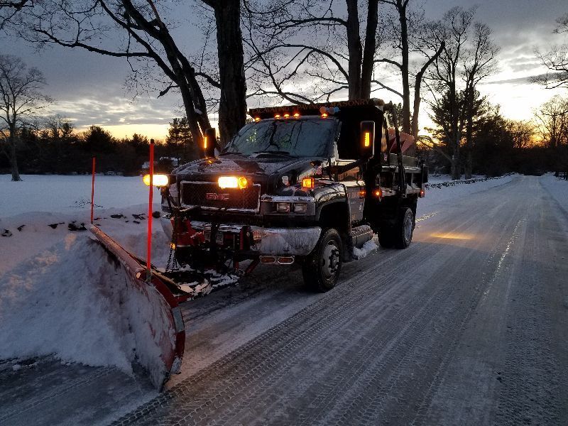 A GMC truck is plowing snow on a snowy road