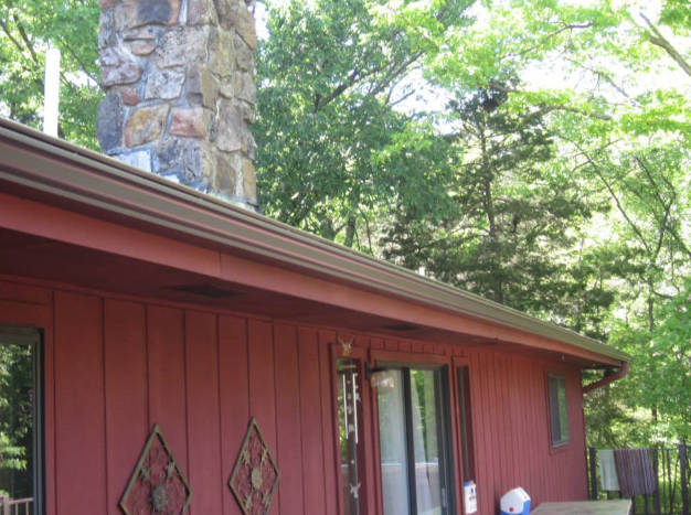 A red house with a stone chimney on the roof surrounded by trees.