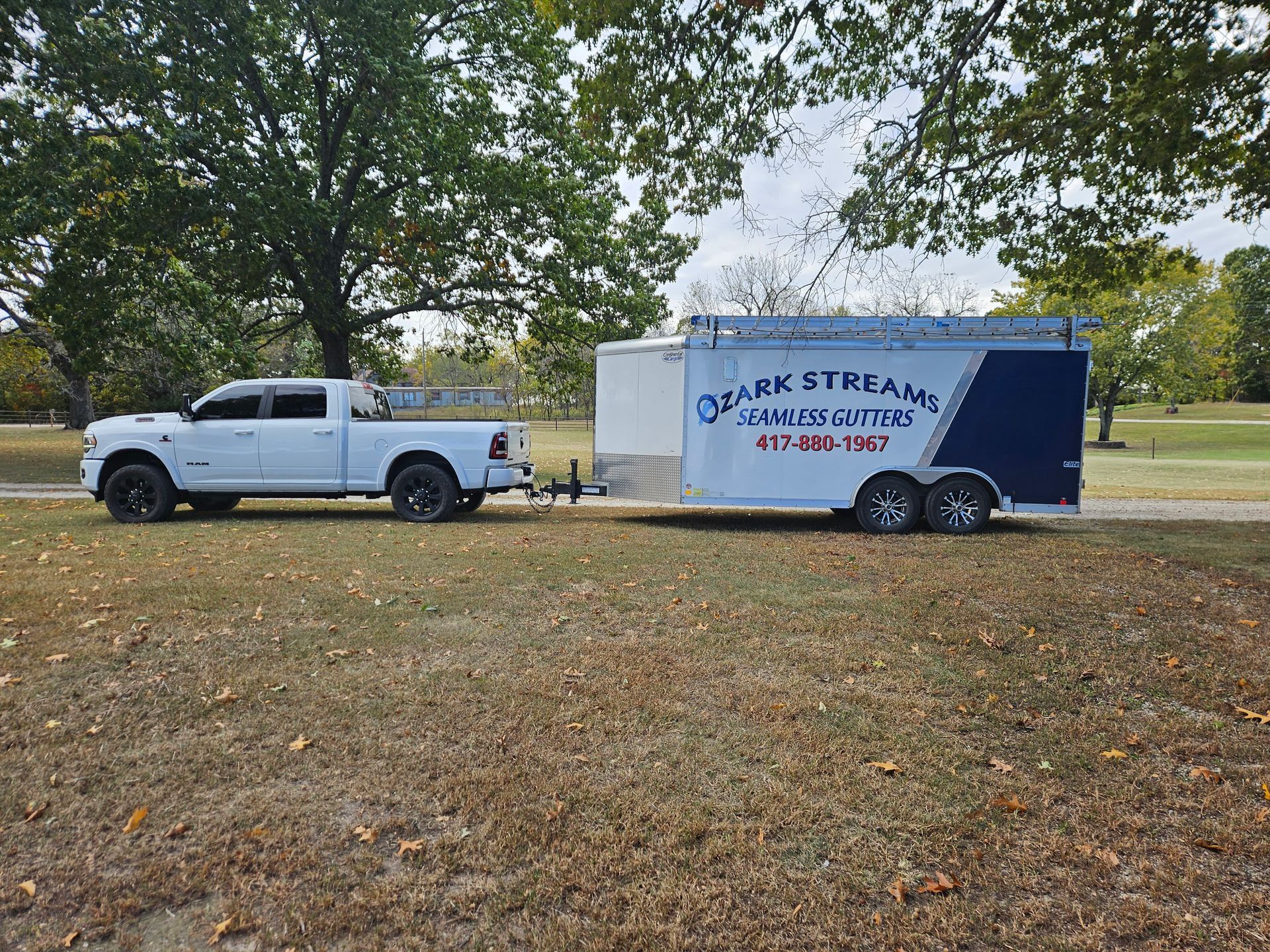 A white truck is towing a trailer in a park.