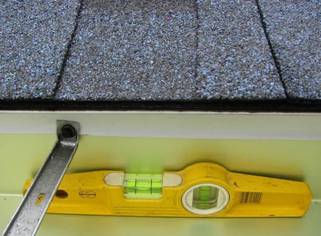 A yellow level is sitting on a wall next to a roof.