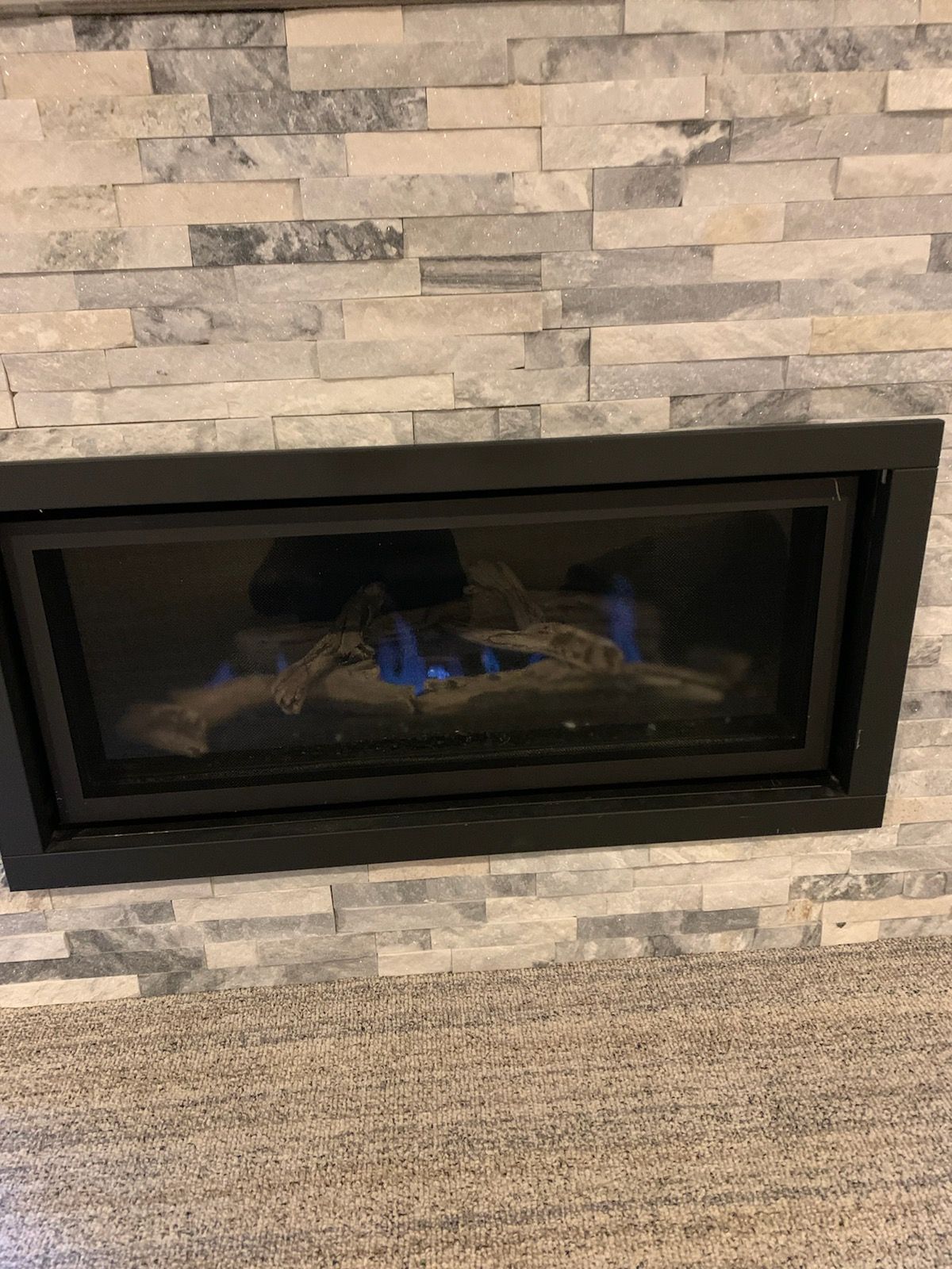 Modern black fireplace set in a stone wall, with a carpeted floor below